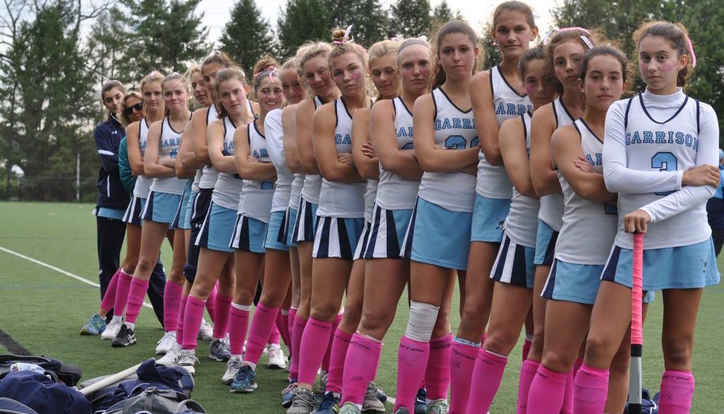 High School Field Hockey Team stands in a line with pink socks for breast cancer awareness