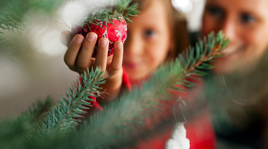 Mother and daughter hang a red ornament on a Christmas tree