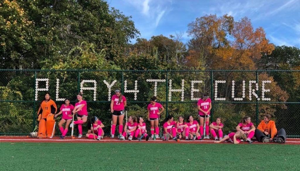 The Gunnery School Field Hockey pose in pink in front of the fence they put cups in to spell out Play4TheCure