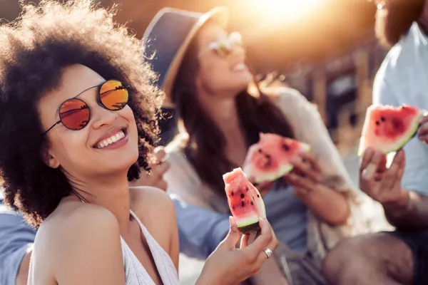 Cheerful young friends eating watermelon on beach,having fun together.
